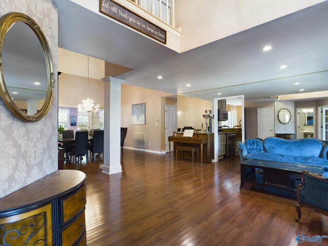 living room featuring dark wood-type flooring, decorative columns, and a notable chandelier