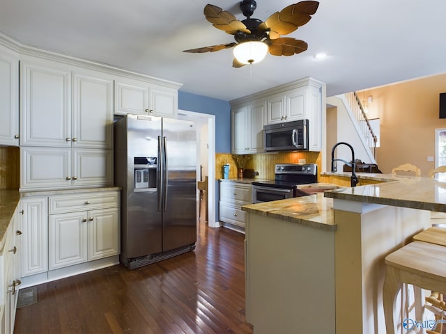 kitchen with a breakfast bar area, dark hardwood / wood-style floors, backsplash, stainless steel appliances, and ceiling fan