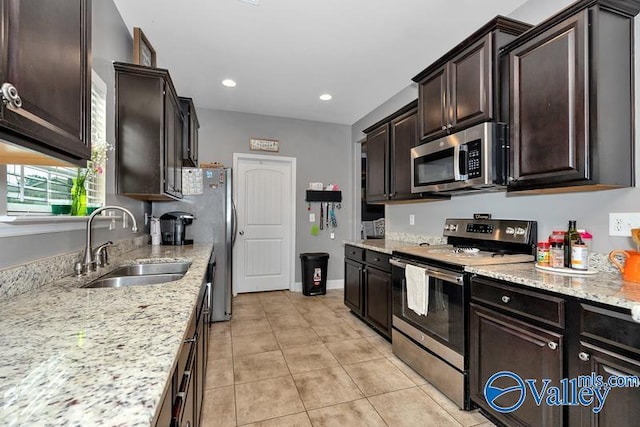 kitchen featuring appliances with stainless steel finishes, sink, light tile patterned floors, light stone counters, and dark brown cabinets