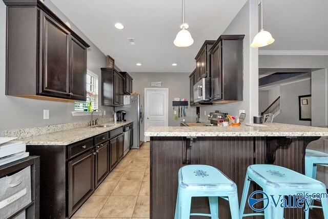 kitchen with appliances with stainless steel finishes, sink, hanging light fixtures, light tile patterned floors, and light stone countertops