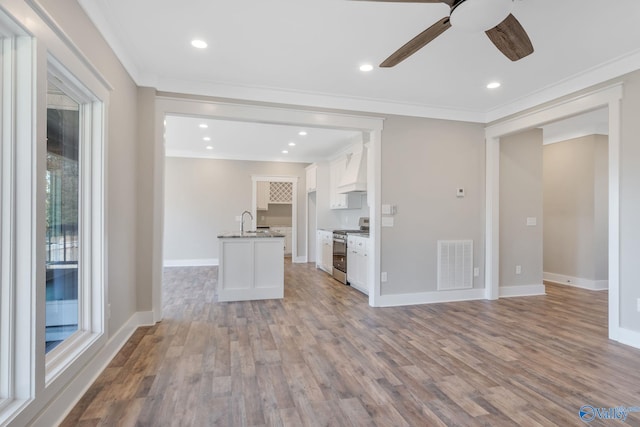 kitchen featuring gas stove, an island with sink, light wood-type flooring, white cabinets, and ornamental molding