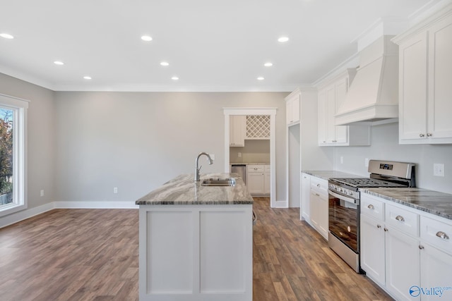 kitchen featuring custom exhaust hood, light stone counters, an island with sink, and gas range