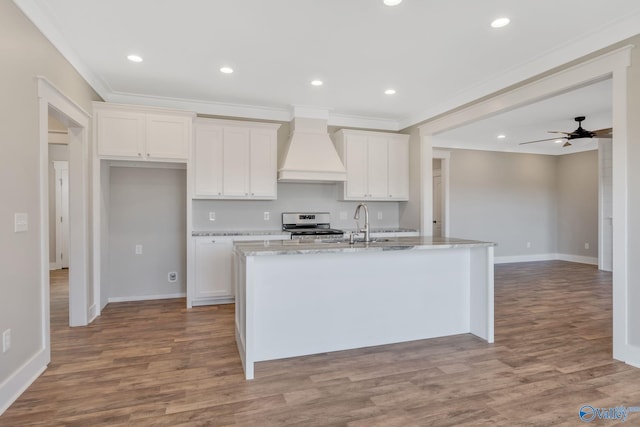 kitchen with custom exhaust hood, ceiling fan, a center island with sink, hardwood / wood-style floors, and white stove