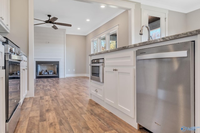 kitchen featuring appliances with stainless steel finishes, a large fireplace, white cabinetry, and light stone counters