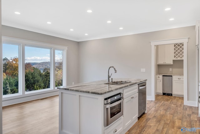 kitchen with appliances with stainless steel finishes, sink, a center island with sink, light hardwood / wood-style flooring, and white cabinets