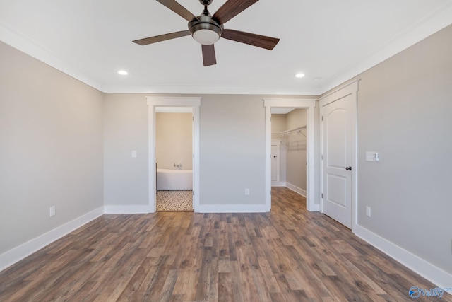 unfurnished bedroom with dark wood-type flooring, ceiling fan, a spacious closet, connected bathroom, and a closet