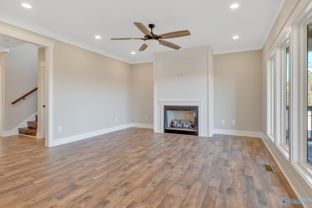 unfurnished living room featuring ceiling fan, a large fireplace, wood-type flooring, and ornamental molding