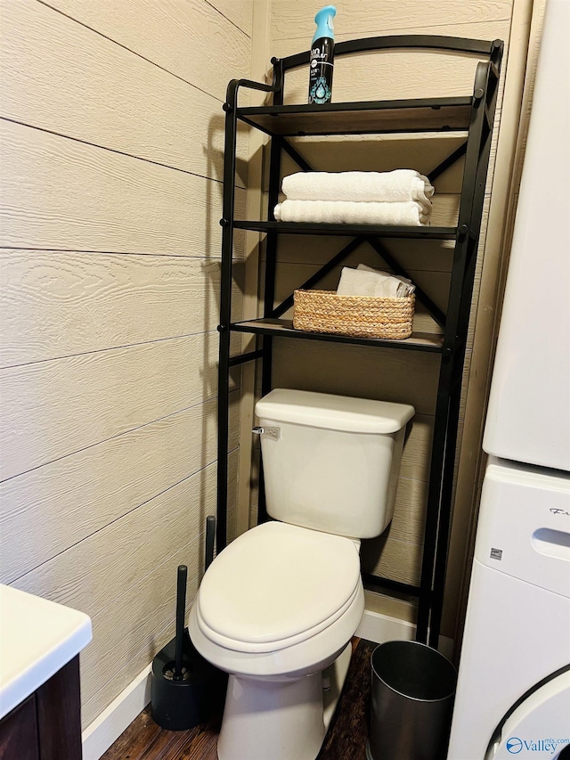 bathroom featuring vanity, wood walls, toilet, stacked washing maching and dryer, and wood-type flooring