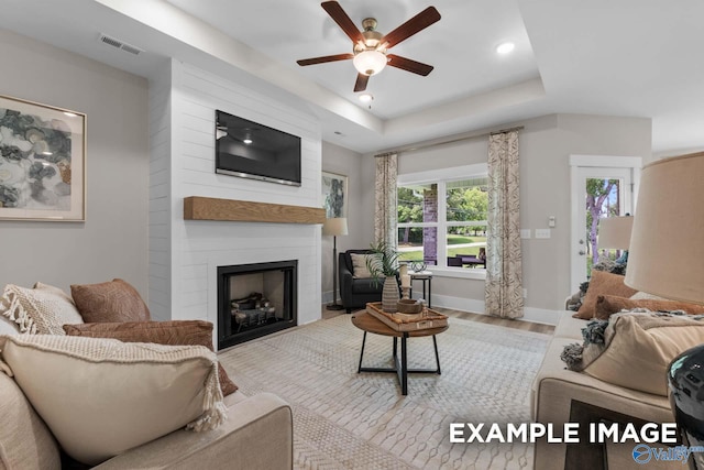 living room featuring a large fireplace, a tray ceiling, ceiling fan, and hardwood / wood-style flooring