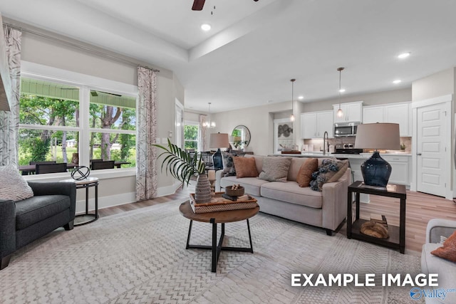 living room with ceiling fan with notable chandelier, light wood-type flooring, and sink