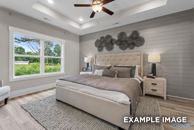 bedroom featuring light hardwood / wood-style flooring, a tray ceiling, and ceiling fan