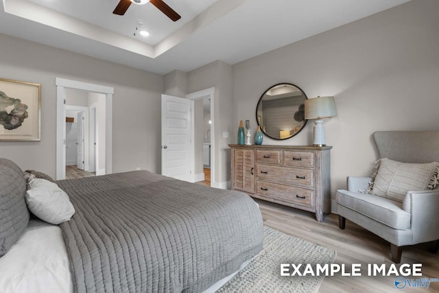 bedroom featuring connected bathroom, ceiling fan, light hardwood / wood-style floors, and a tray ceiling