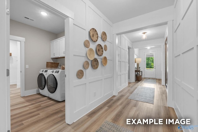 clothes washing area featuring washer and clothes dryer, light wood-type flooring, and cabinets