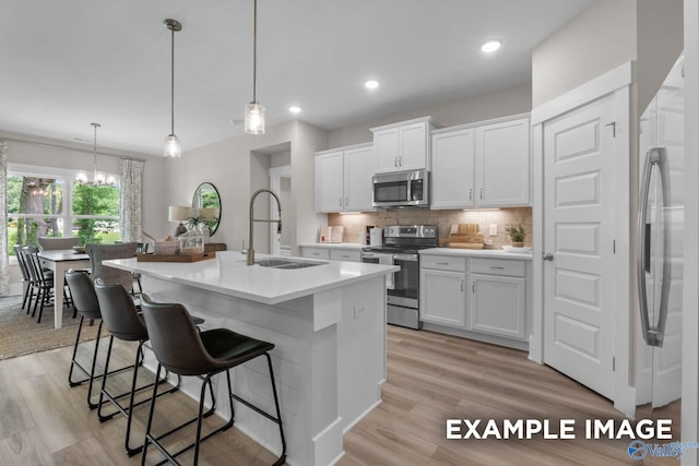 kitchen with decorative backsplash, appliances with stainless steel finishes, sink, white cabinetry, and light hardwood / wood-style floors