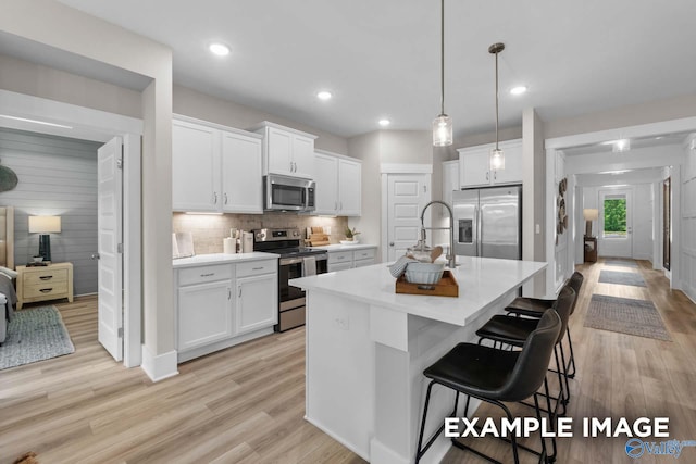 kitchen featuring stainless steel appliances, white cabinets, light wood-type flooring, a kitchen bar, and a center island with sink