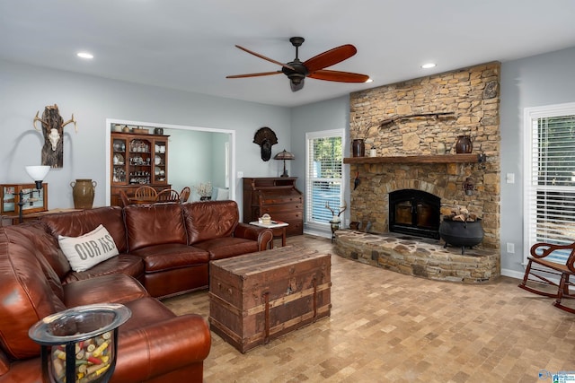 living room featuring ceiling fan, a stone fireplace, and a wealth of natural light