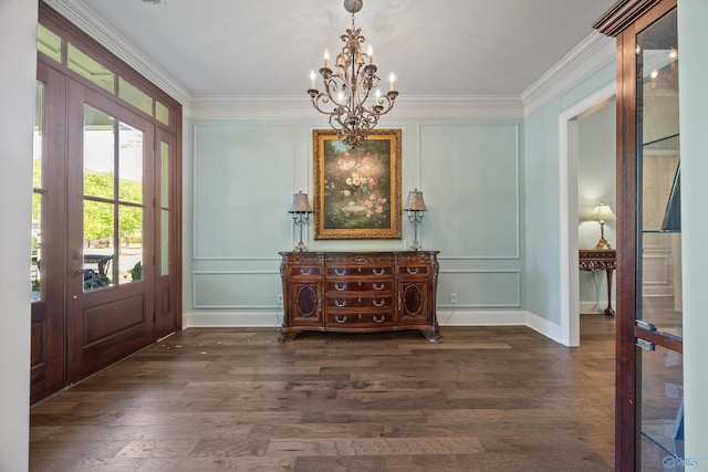entryway with an inviting chandelier, crown molding, a decorative wall, and dark wood finished floors