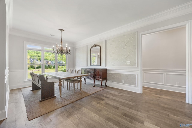 dining space featuring ornamental molding, a decorative wall, wood finished floors, and a chandelier