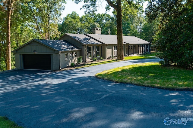 view of front of home with a chimney, brick siding, aphalt driveway, a front lawn, and an attached garage