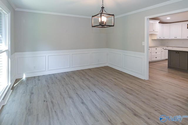 unfurnished dining area featuring an inviting chandelier, light wood-type flooring, ornamental molding, and wainscoting