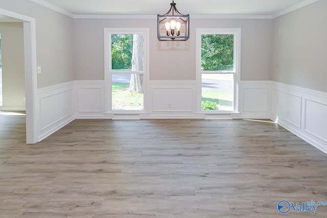 unfurnished dining area featuring a chandelier, crown molding, and a wainscoted wall