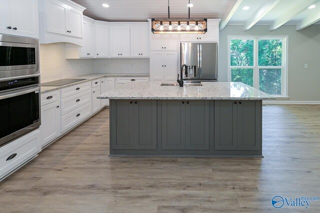 kitchen featuring stainless steel appliances, beamed ceiling, light stone countertops, a center island with sink, and light hardwood / wood-style flooring