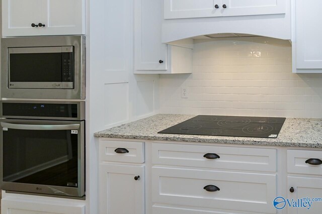 kitchen featuring white cabinetry, tasteful backsplash, premium range hood, light stone countertops, and appliances with stainless steel finishes