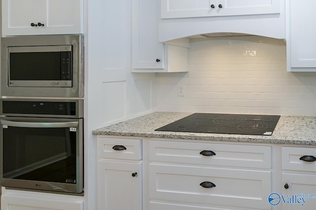 kitchen with stainless steel appliances, tasteful backsplash, light stone counters, premium range hood, and white cabinets