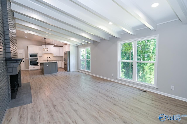 unfurnished living room featuring a sink, visible vents, baseboards, light wood finished floors, and vaulted ceiling with beams