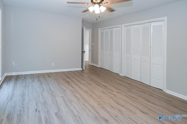 unfurnished bedroom featuring a ceiling fan, wood finished floors, multiple closets, and baseboards