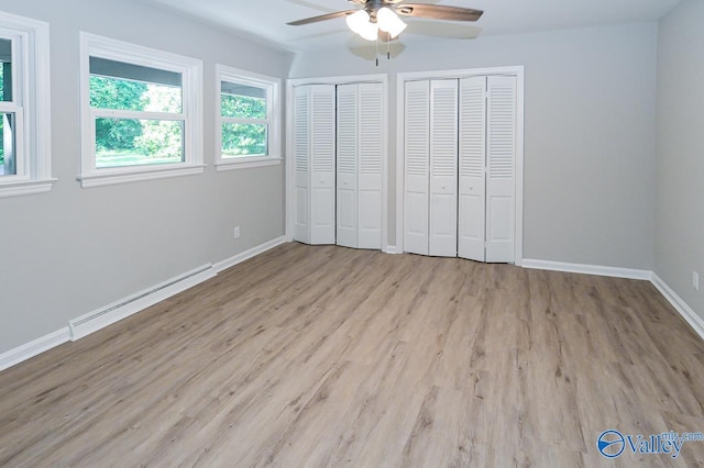 unfurnished bedroom featuring wood finished floors, a baseboard heating unit, multiple closets, ceiling fan, and baseboards