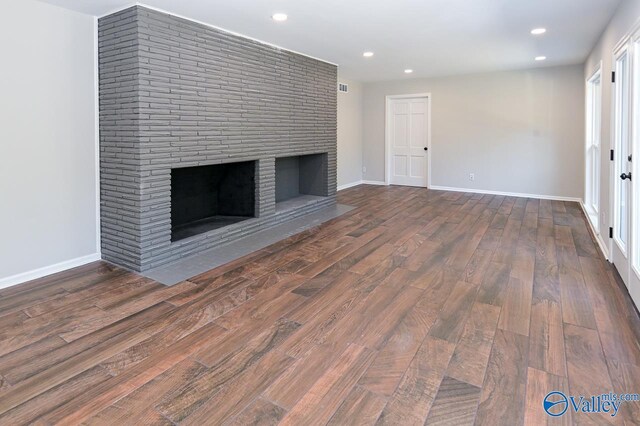 unfurnished living room with brick wall, wood-type flooring, and a brick fireplace