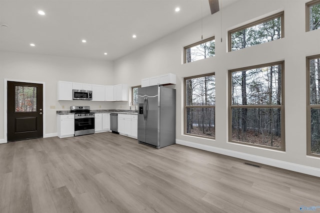 kitchen featuring white cabinetry, light hardwood / wood-style floors, a high ceiling, and appliances with stainless steel finishes