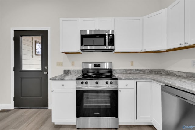 kitchen with stainless steel appliances, white cabinetry, and light stone counters