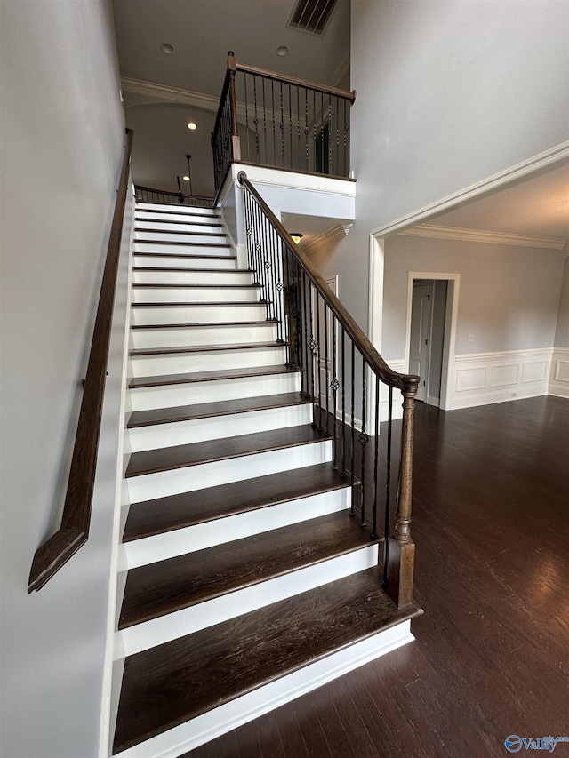 staircase featuring wood-type flooring, a towering ceiling, and crown molding