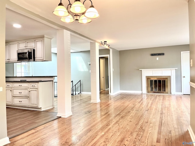 unfurnished living room featuring light wood-style floors, a glass covered fireplace, baseboards, and an inviting chandelier