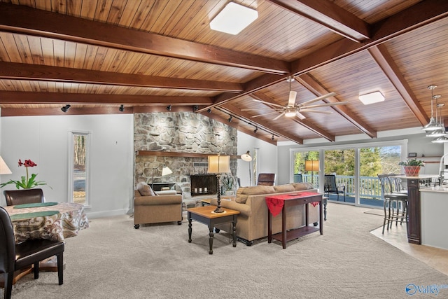 living room with rail lighting, ceiling fan, lofted ceiling with beams, wooden ceiling, and a stone fireplace