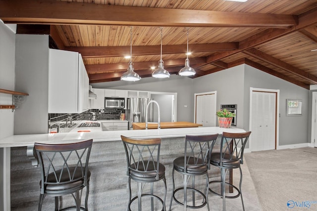 kitchen featuring hanging light fixtures, vaulted ceiling with beams, appliances with stainless steel finishes, white cabinetry, and kitchen peninsula