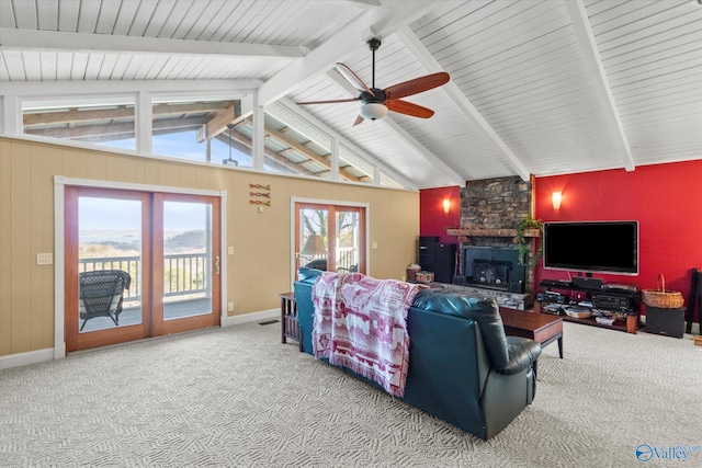 carpeted living room with vaulted ceiling with beams, ceiling fan, a stone fireplace, and french doors