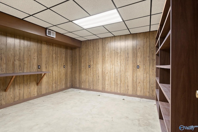 basement featuring wood walls and a drop ceiling