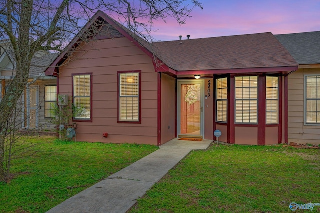 view of front facade with a yard and a shingled roof