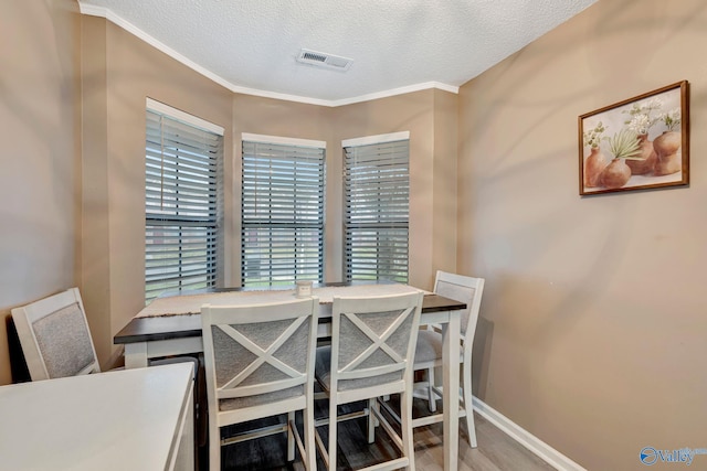 dining area featuring crown molding, visible vents, a textured ceiling, wood finished floors, and baseboards