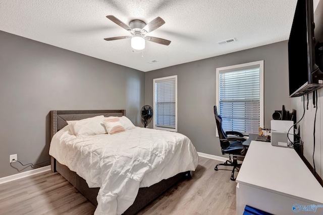 bedroom featuring a textured ceiling, ceiling fan, visible vents, baseboards, and light wood-type flooring