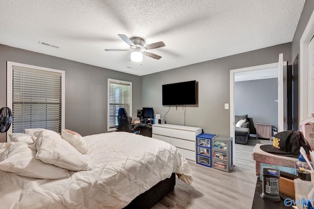 bedroom featuring a textured ceiling, ceiling fan, visible vents, and light wood-style floors