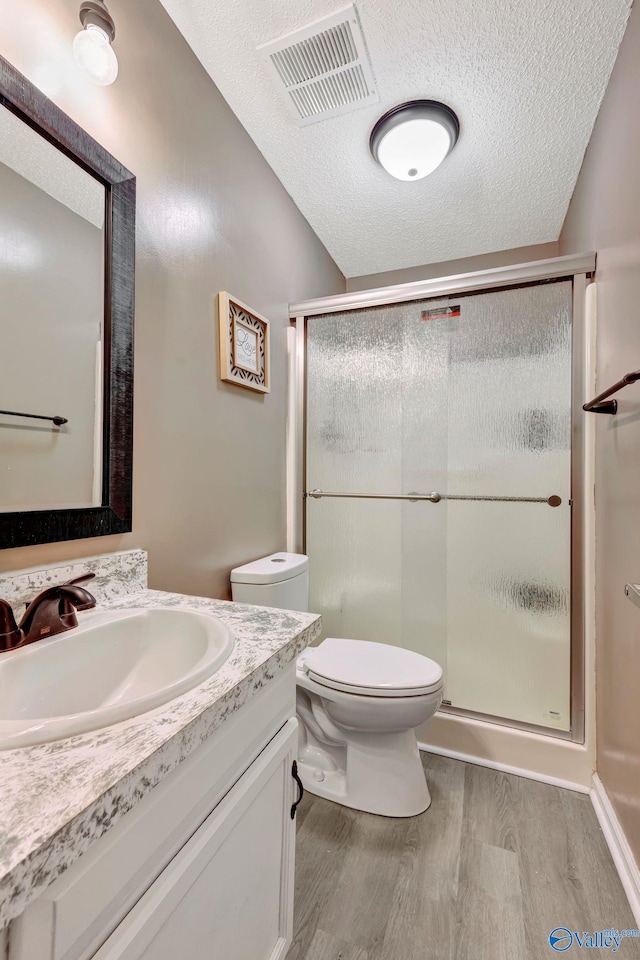 full bathroom featuring a textured ceiling, toilet, wood finished floors, visible vents, and a shower stall