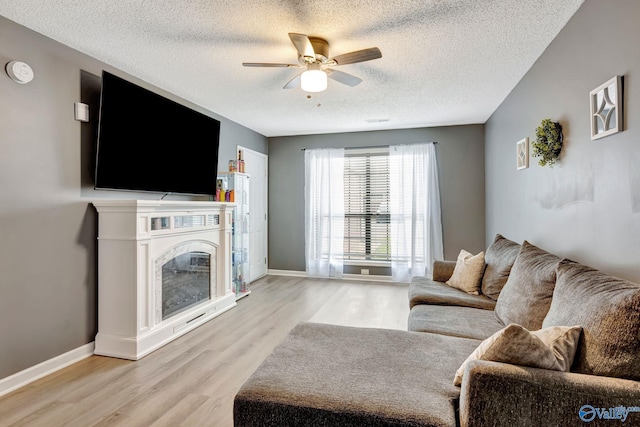 living room featuring baseboards, a glass covered fireplace, a ceiling fan, and light wood-style floors