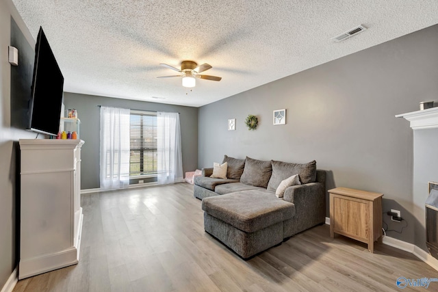 living area featuring baseboards, light wood-style flooring, visible vents, and a ceiling fan