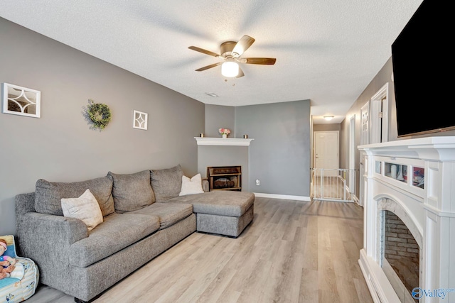 living area featuring a fireplace, light wood-style floors, ceiling fan, a textured ceiling, and baseboards