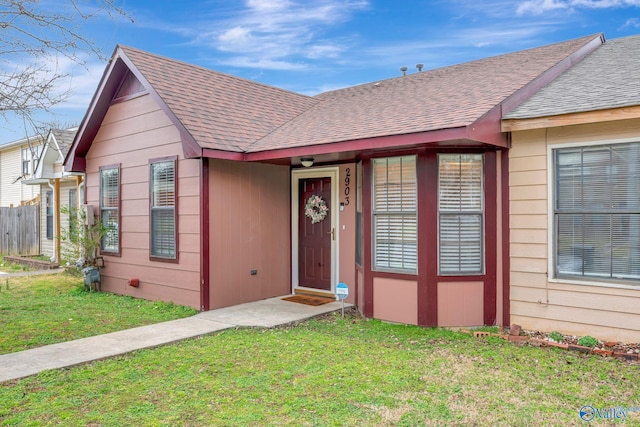 ranch-style house with roof with shingles, fence, and a front lawn