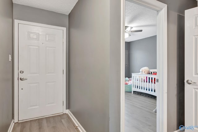 doorway to outside with a textured ceiling, light wood-type flooring, a ceiling fan, and baseboards